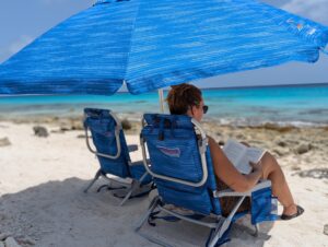 Relaxing on a Bonaire beach with rented beach chairs and a blue umbrella from Joor Beach Rentals, overlooking the turquoise ocean