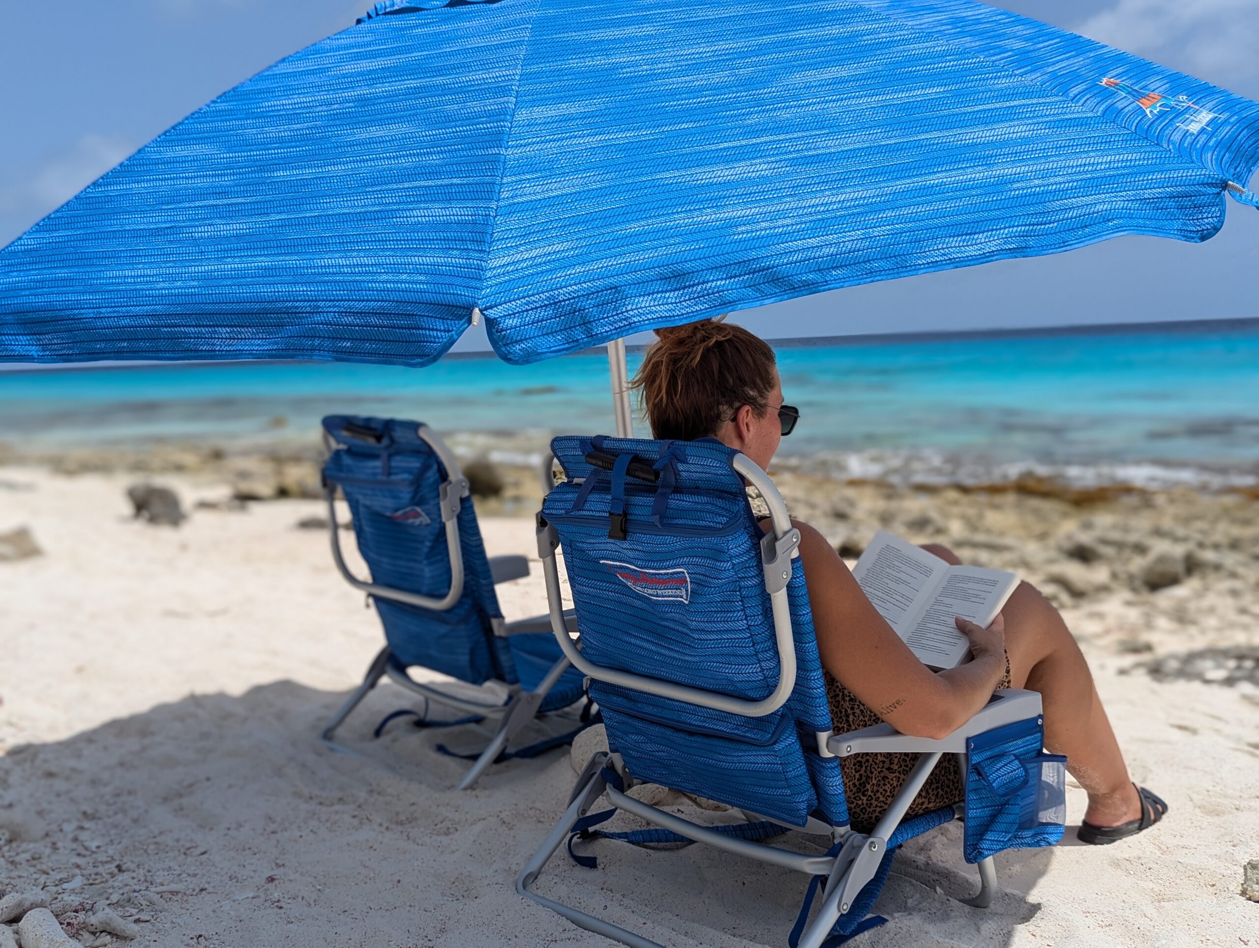 Relaxing on a Bonaire beach with rented beach chairs and a blue umbrella from Joor Beach Rentals, overlooking the turquoise ocean